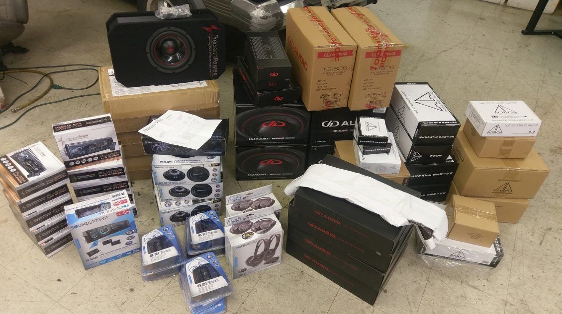 Boxed electronics and accessories stacked on a floor, with a speaker, cardboard packages, and foam packaging.