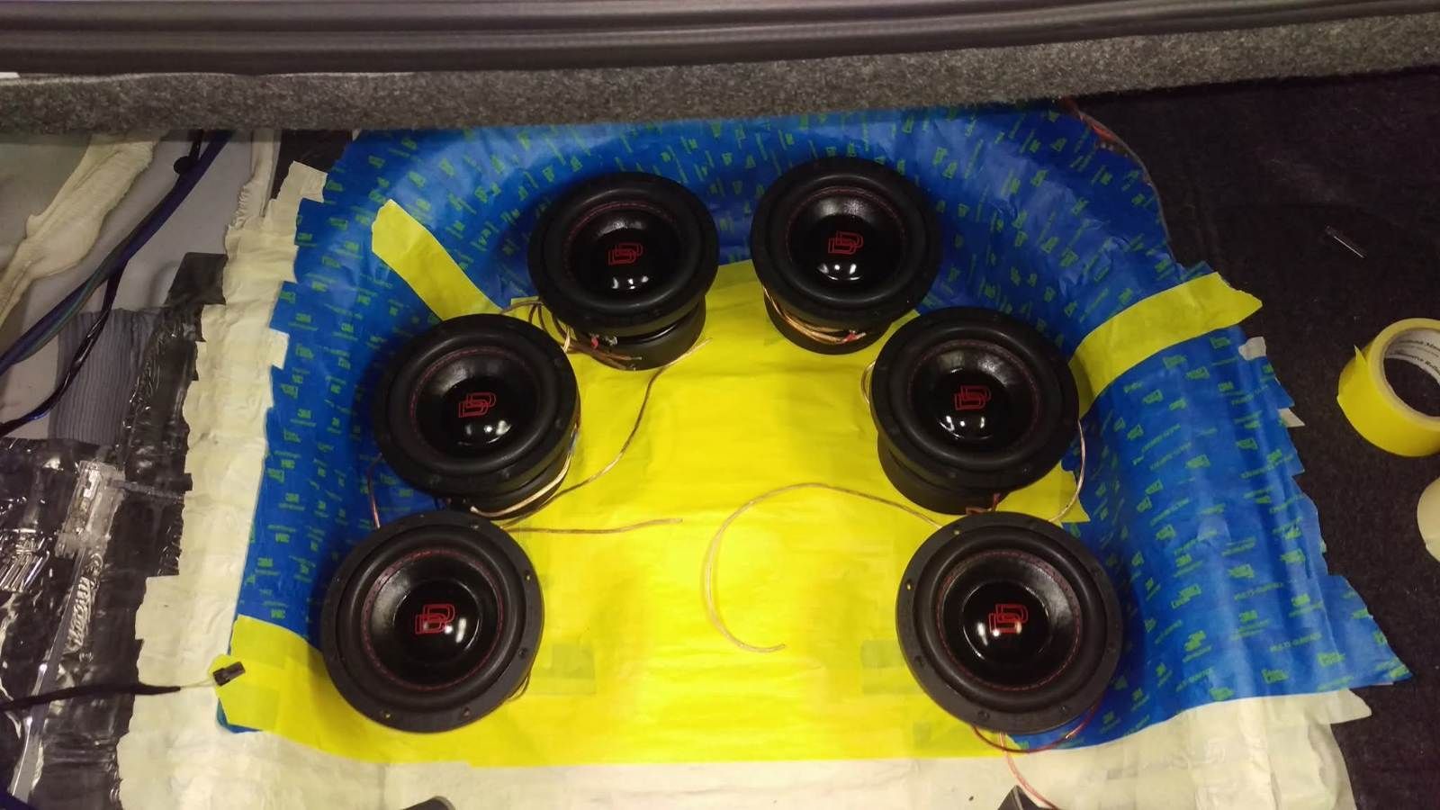 Six black speaker drivers arranged on a yellow board with blue padding around it