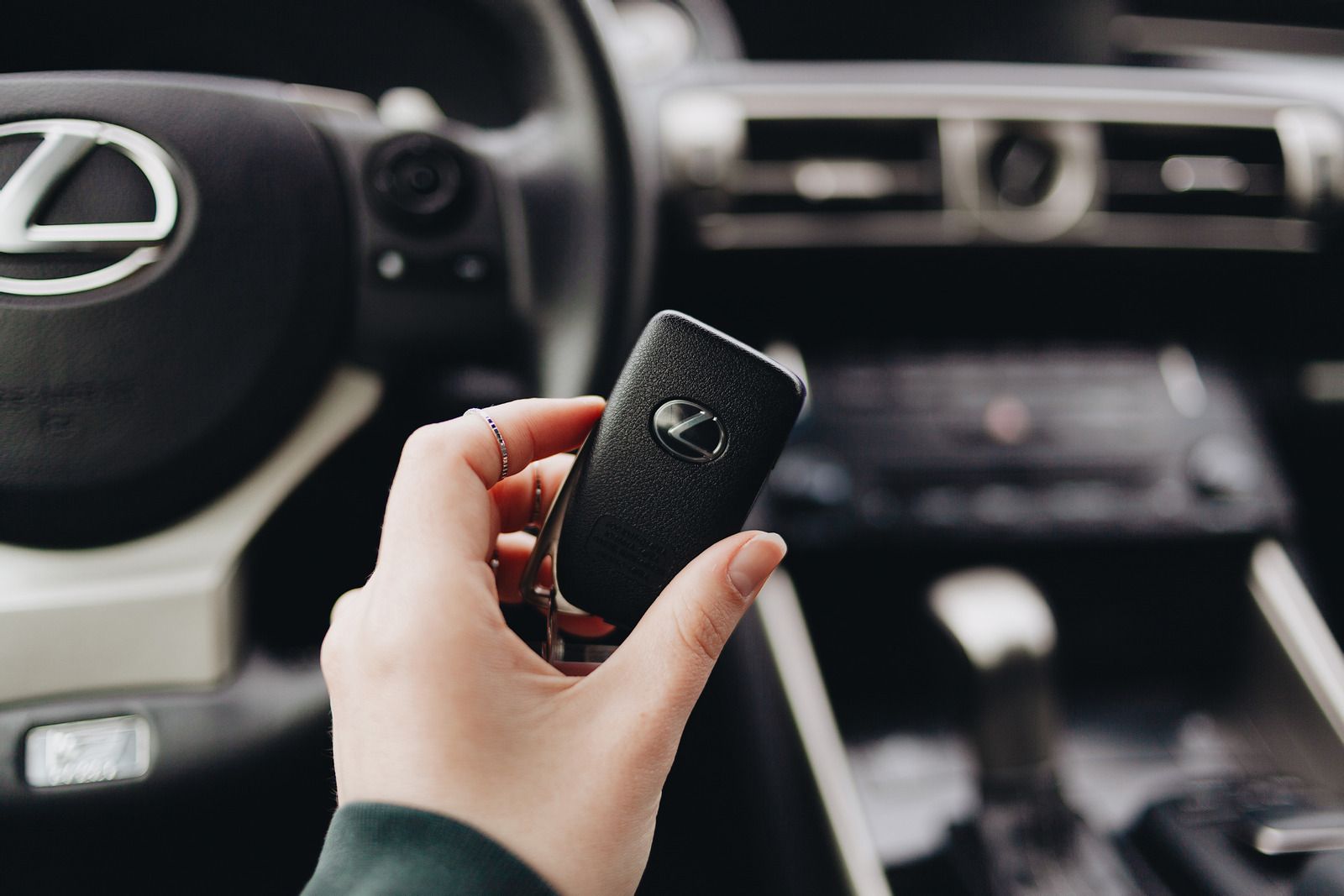 Hand holding a Lexus key fob inside a car, with the steering wheel and dashboard in view