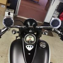 View from a motorcycle cockpit showing chrome handlebars, mirrors, and a speedometer on a black fuel tank.