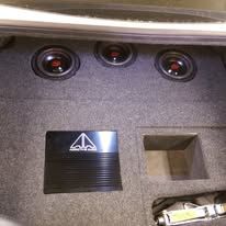 Car audio enclosure with three speakers and a black JL Audio subwoofer in a gray carpeted trunk