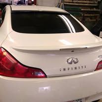 White Infiniti sedan viewed from the rear in a garage, with red taillights and trunk badge visible