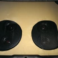 Black mesh speaker grilles mounted on a tan panel, side by side