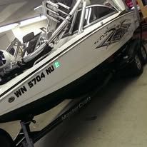 White speedboat on a trailer in a garage, with black registration number and chrome railings.