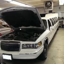 White stretch limousine in a garage with its hood open, showing the engine compartment.