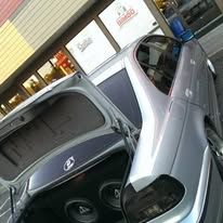 Silver car with open trunk parked beside a storefront at a gas station
