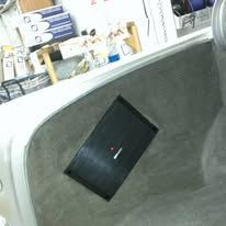 Black rectangular device sitting at an angle inside a gray container, with shelves in the background