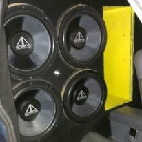 Four black speakers with triangular logos mounted beside a bright yellow panel in a vehicle or audio setup