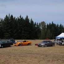 Three sports cars parked on a dry field near a tent, with trees in the background.