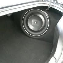 Car trunk with a large round speaker/subwoofer mounted in the side panel.
