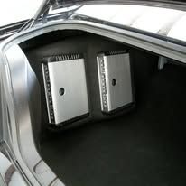 Two silver speaker enclosures installed in the open trunk of a car