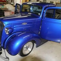 Bright blue classic car parked in a garage, front door open and shiny chrome wheel visible