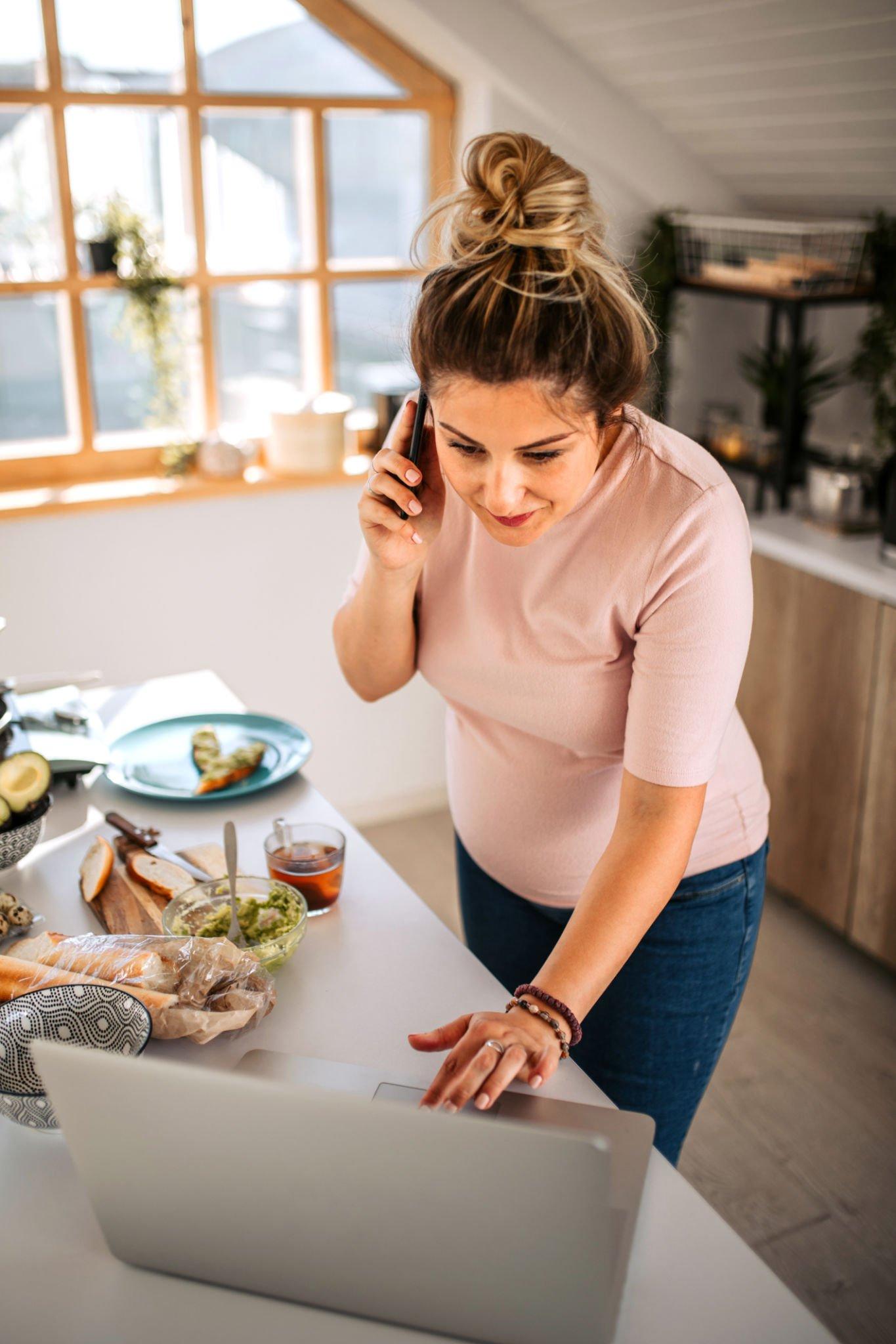 A woman is talking on a cell phone while looking at a laptop.