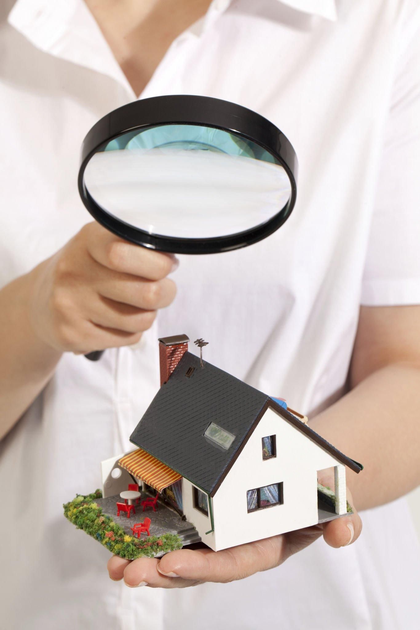 A person is holding a magnifying glass over a model house