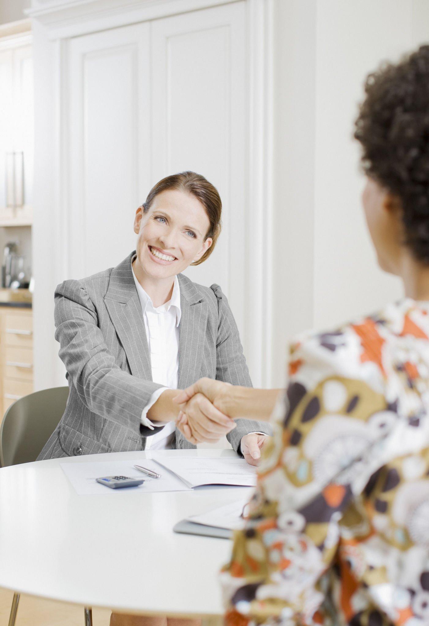 A woman is shaking hands with another woman at a table.