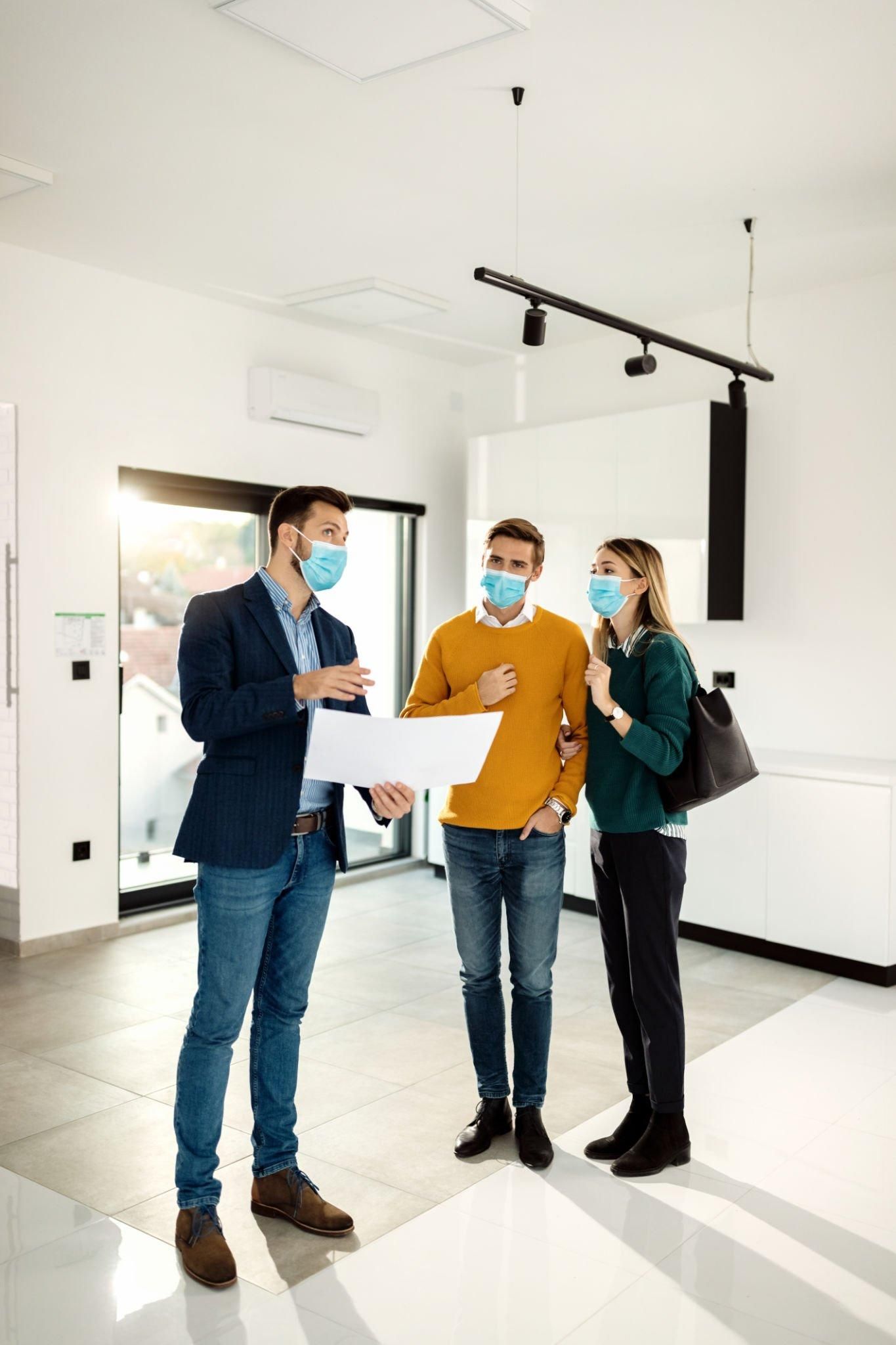A man and a woman wearing face masks are looking at a blueprint in an empty room.