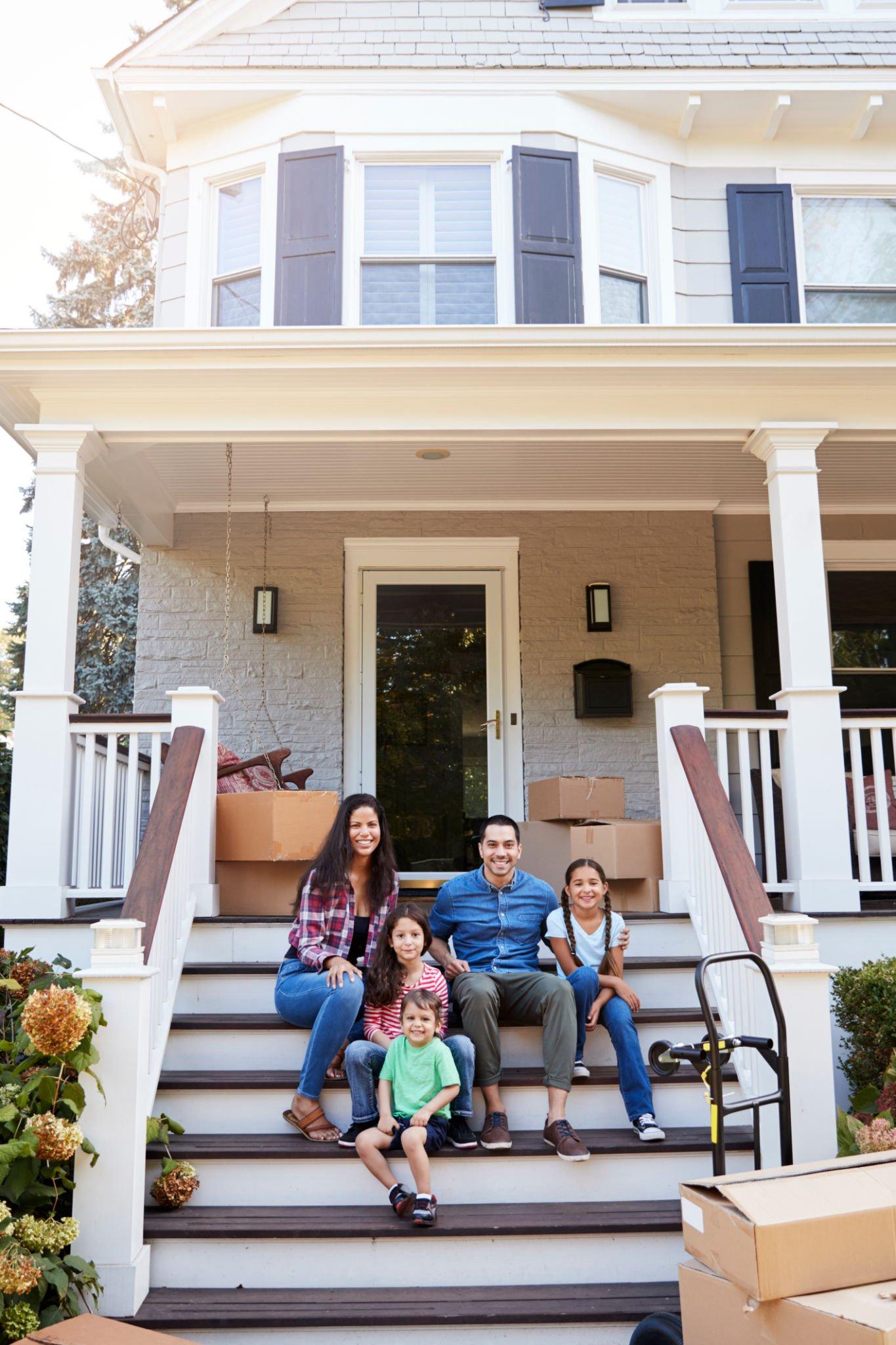 A family is sitting on the steps of their new home.
