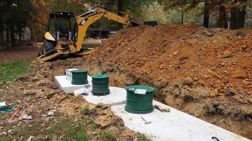 Septic Tanks At A Factory — Mechanicsville, VA — C & W Hanover Septic A small excavator digging near a concrete septic tank with green lids in a yard.