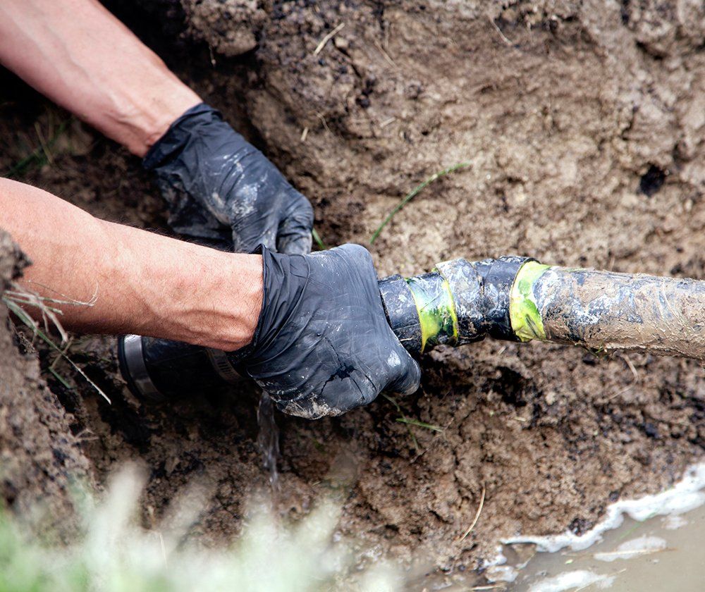 Fixing Underground Pipe — Mechanicsville, VA — C & W Hanover Septic Hands wearing black gloves fixing a broken underground pipe in dirt.