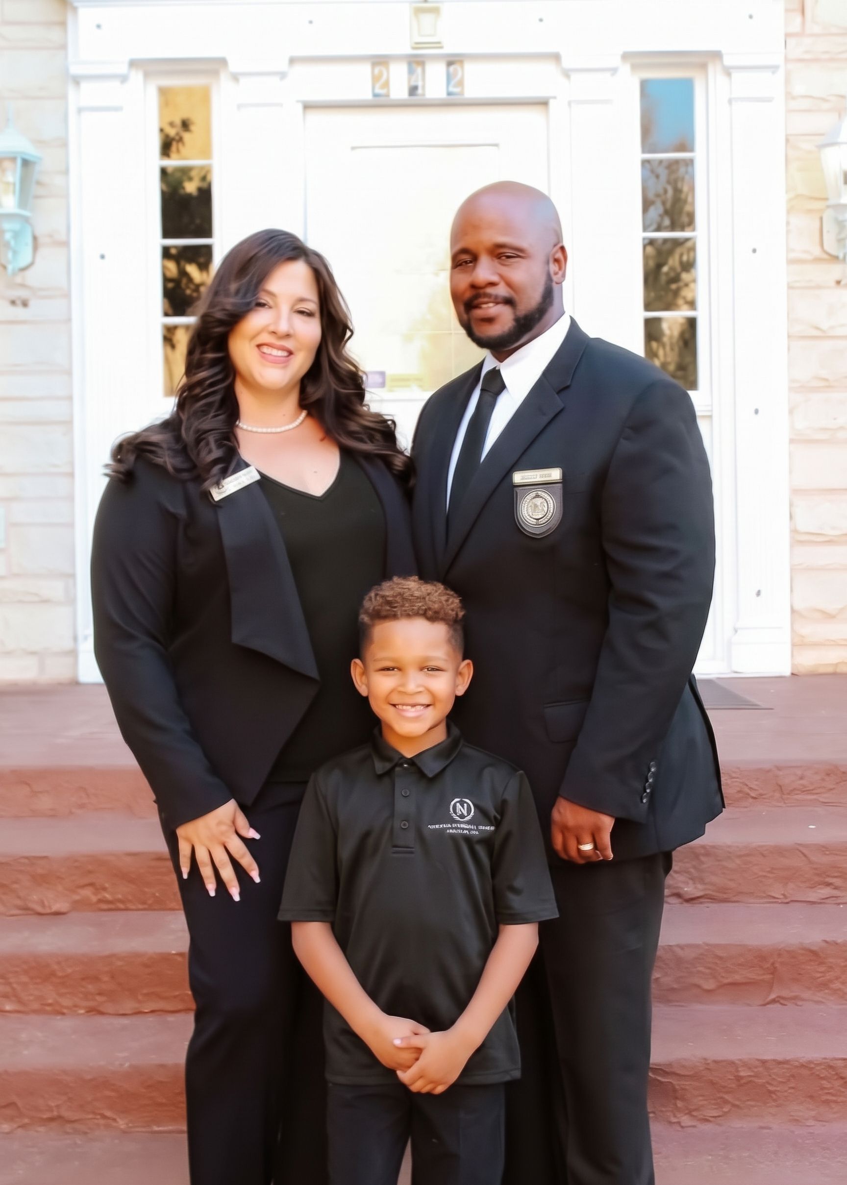 Three people posing on church steps, wearing black formal outfits, smiling at the camera.