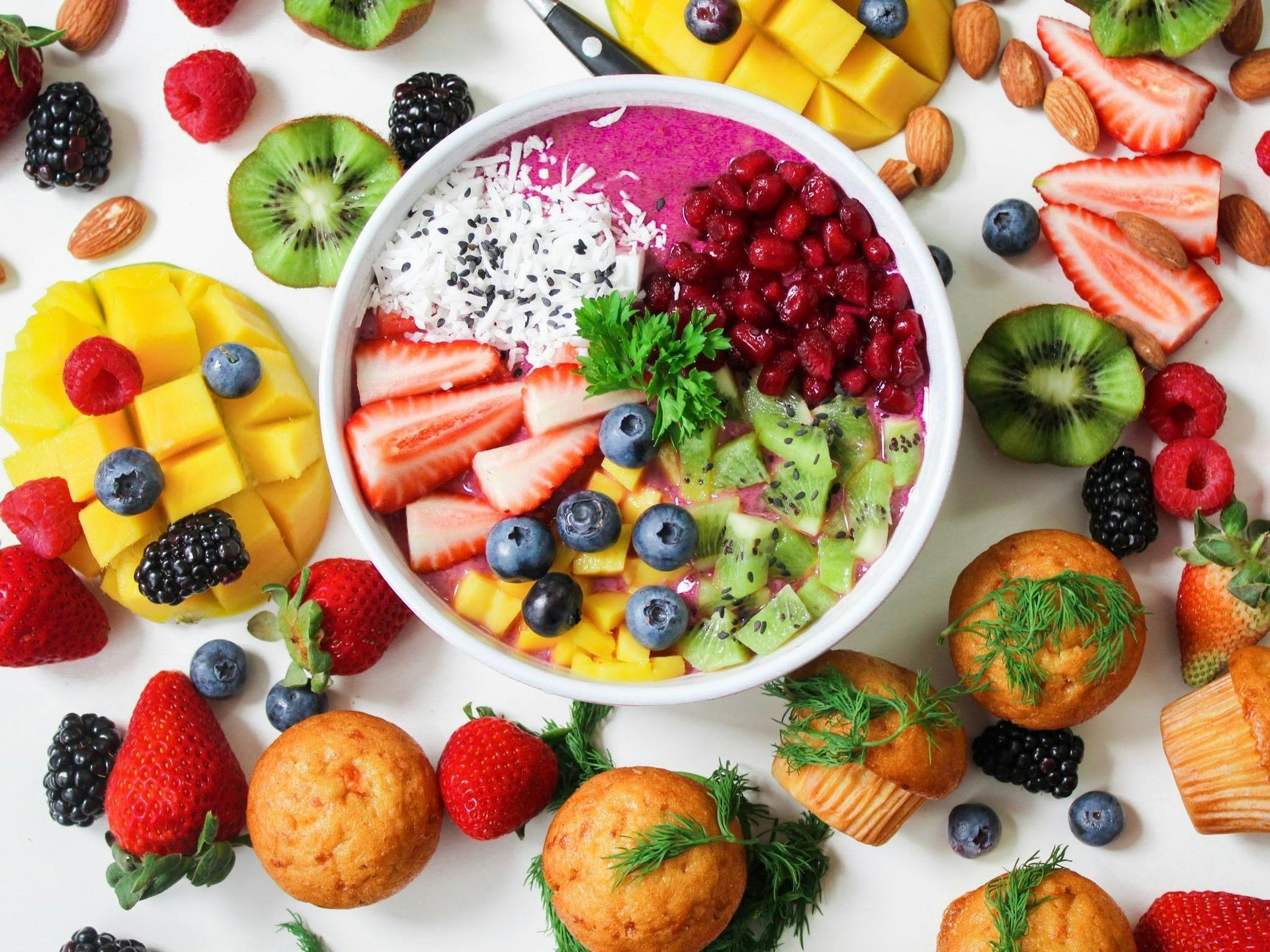 Colorful fruit bowl with berries, mango, kiwi, and muffins.