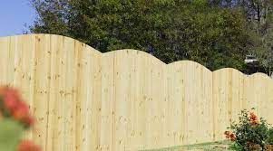 A wooden fence with a curved top is surrounded by trees.