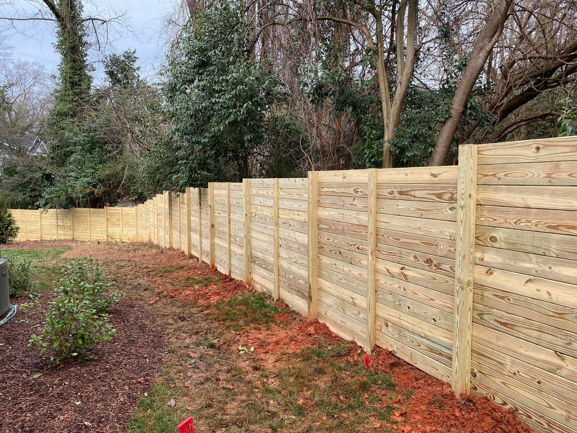 A wooden fence is surrounded by trees in a backyard.