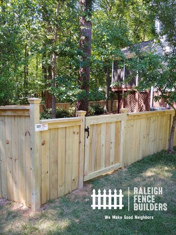 A wooden fence with a gate and trees in the background.