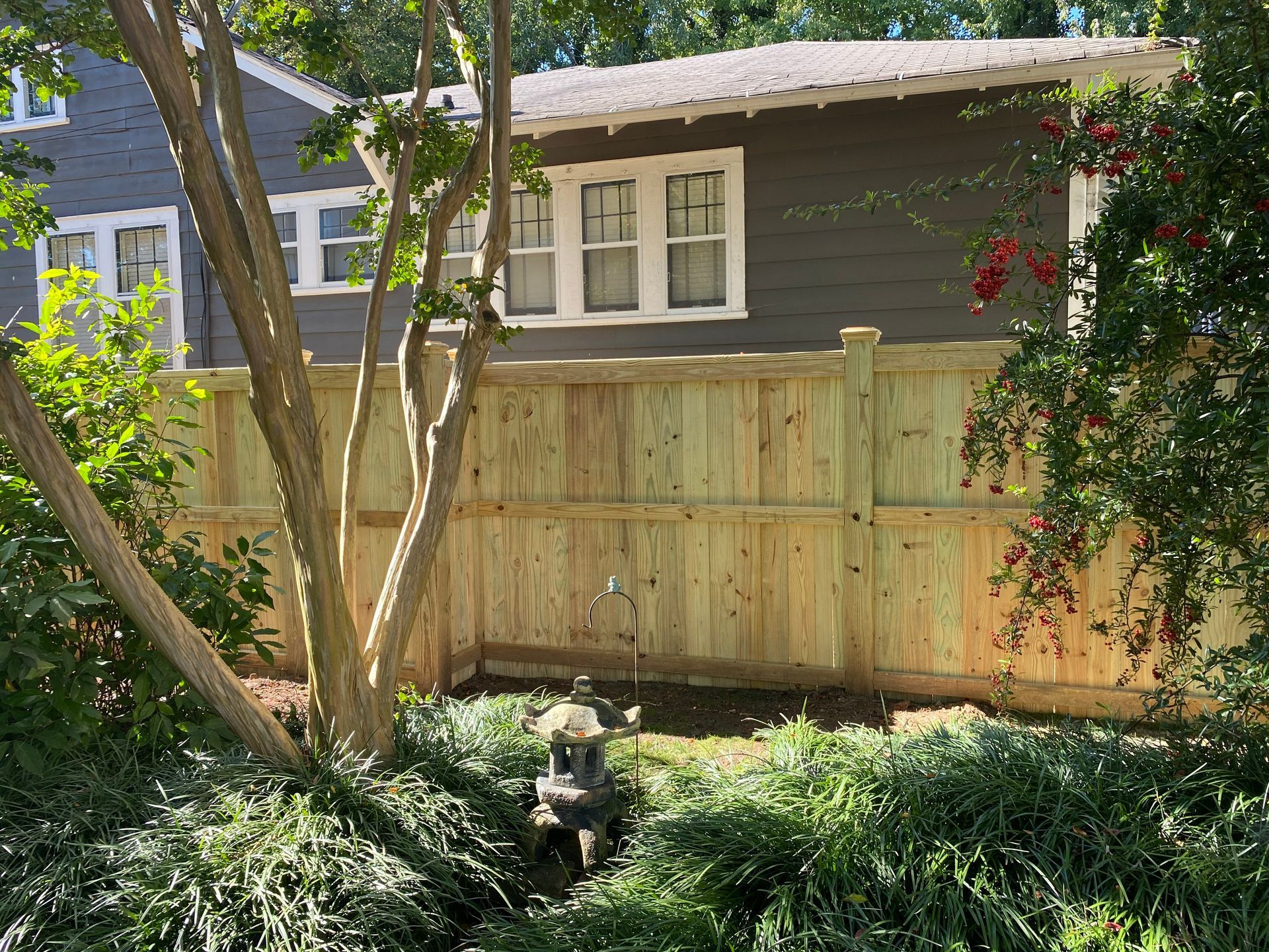 A wooden fence is surrounded by trees and bushes in front of a house.