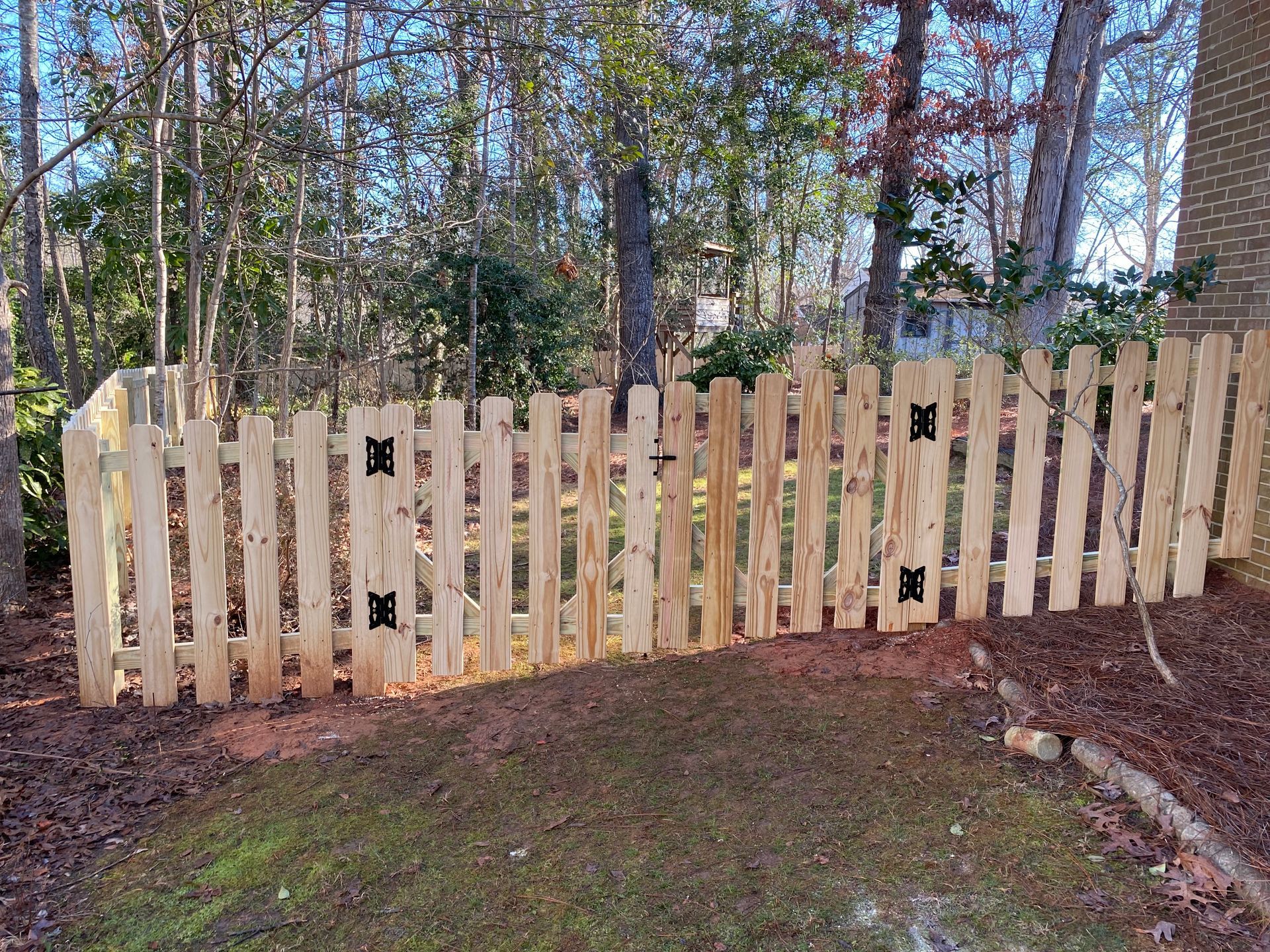 A wooden picket fence is surrounded by trees in a yard.