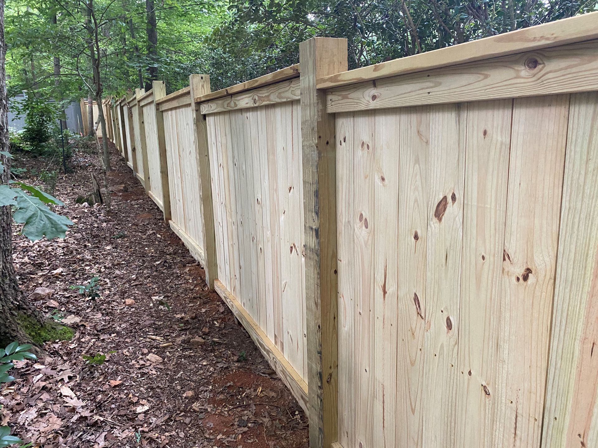 A wooden fence is surrounded by trees and leaves.