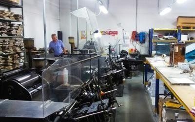Reparto di stampa con grandi macchine da stampa, scaffali e un uomo in piedi sullo sfondo.