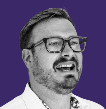 A man with glasses and a beard is smiling in a black and white photo.
