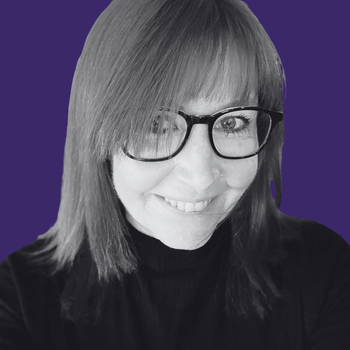 A woman wearing glasses and a black shirt is smiling in a black and white photo.