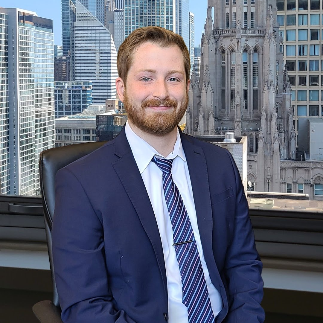 A man in a suit and tie is sitting in front of a window with a city skyline in the background.