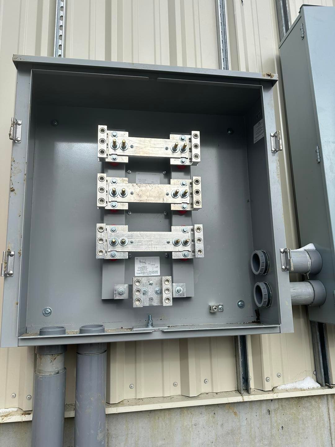 Open metal electrical junction box on a building's exterior, containing busbars and wiring connections.