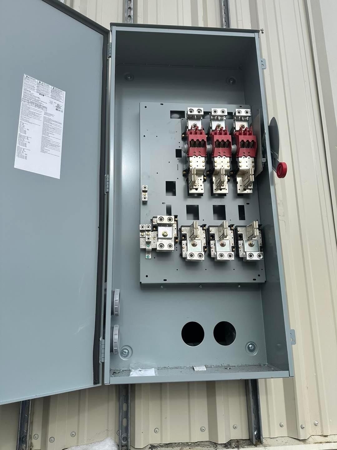 Gray electrical panel with open door, containing red and white circuit breakers.