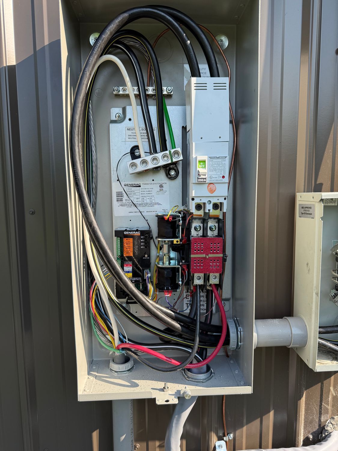 Electrical panel with wires and components, mounted outdoors on a brown building.