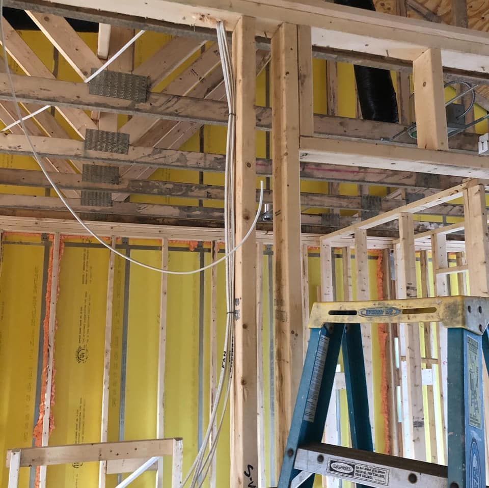 Interior view of a building under construction, showing wooden framing, yellow insulation, and a ladder.