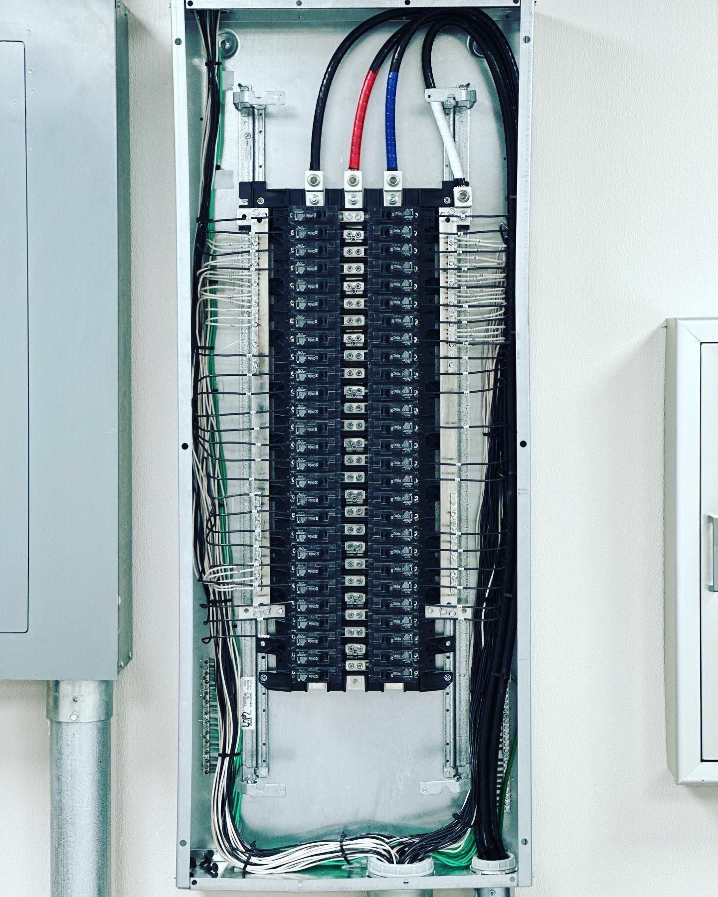 Open electrical panel with black breakers, red, blue, and black wires.
