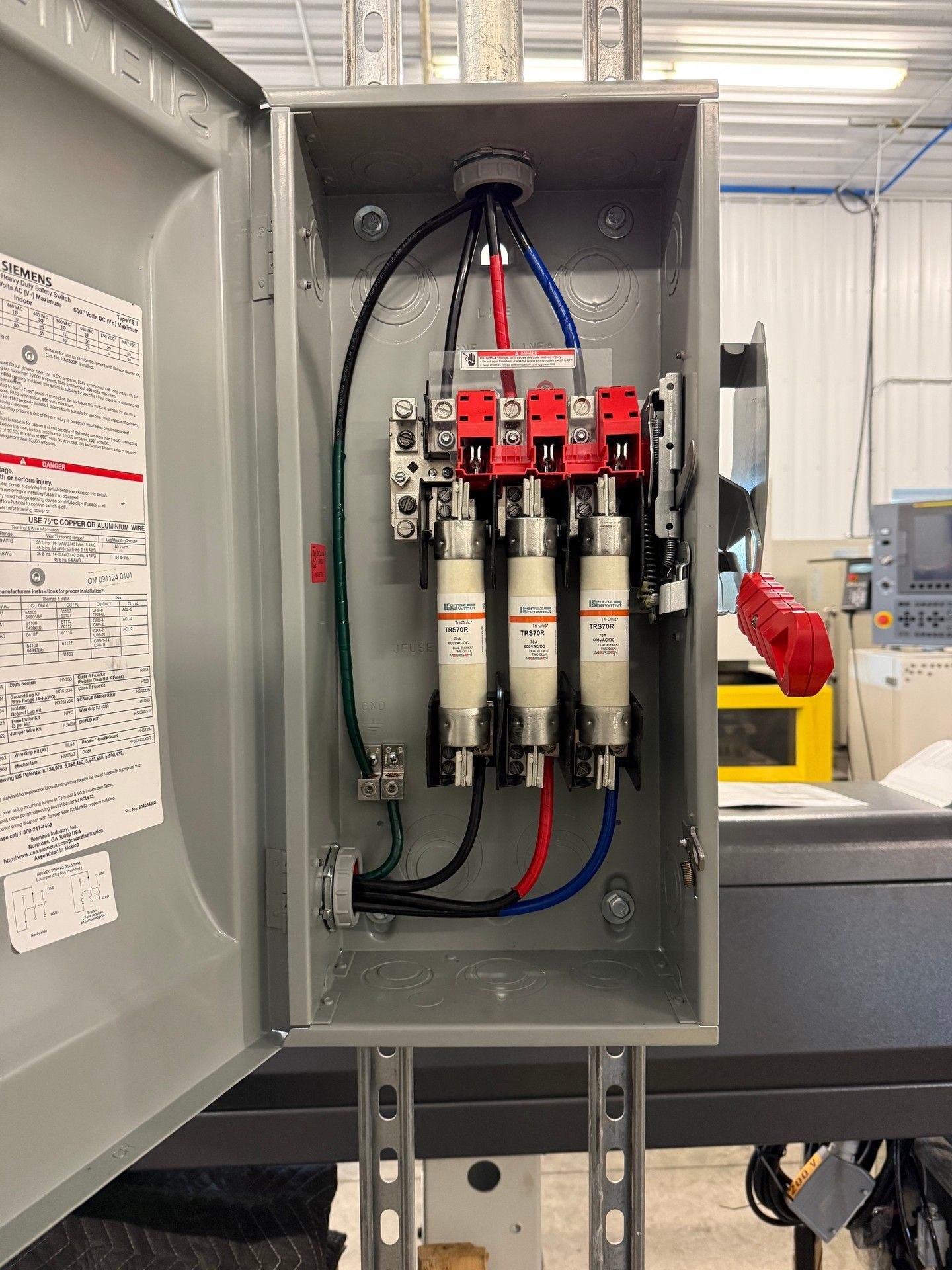 Open electrical fuse box with three fuses, wires, and circuit breakers.