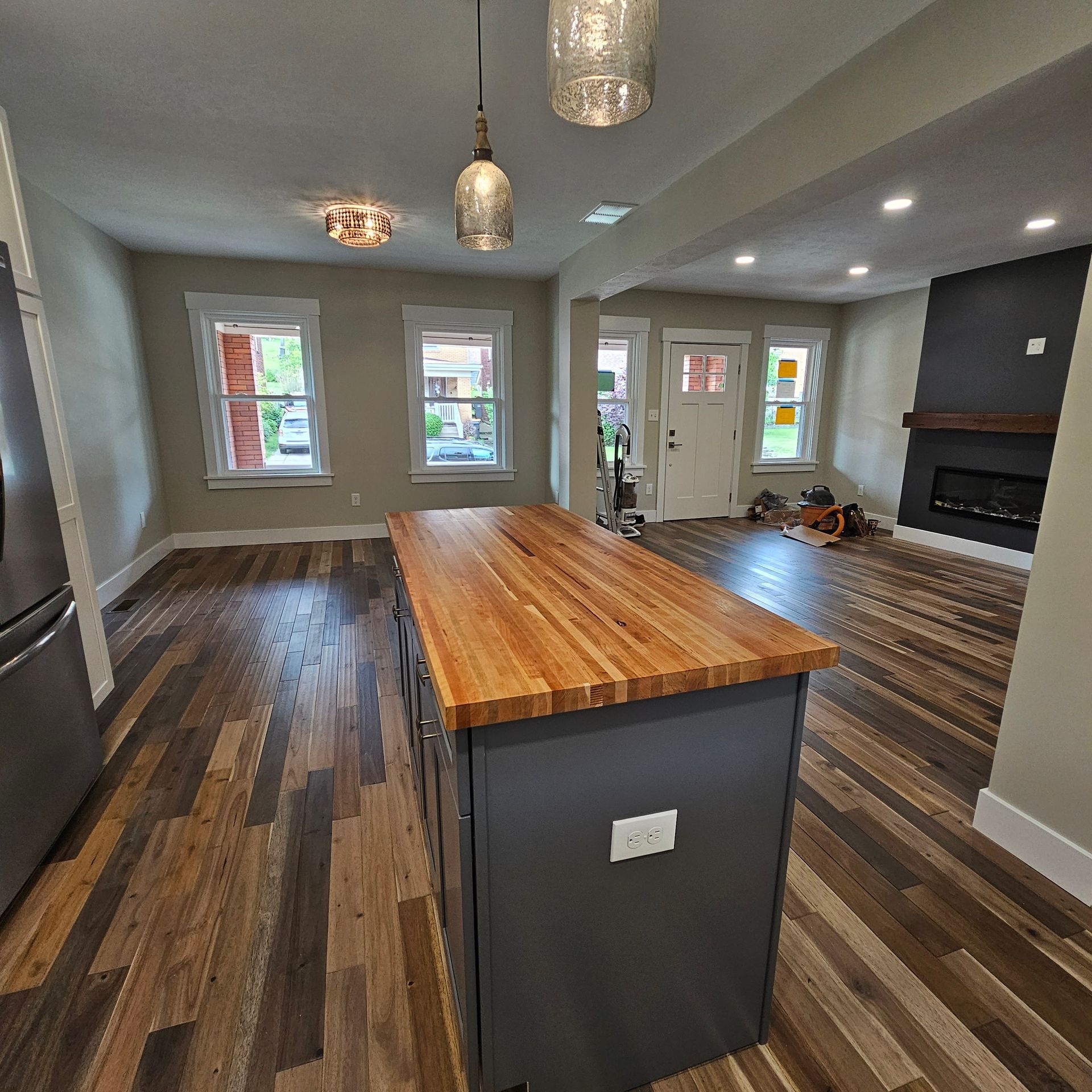 Kitchen with island, wood countertop, gray cabinets, hardwood floor, fireplace, and light fixtures.