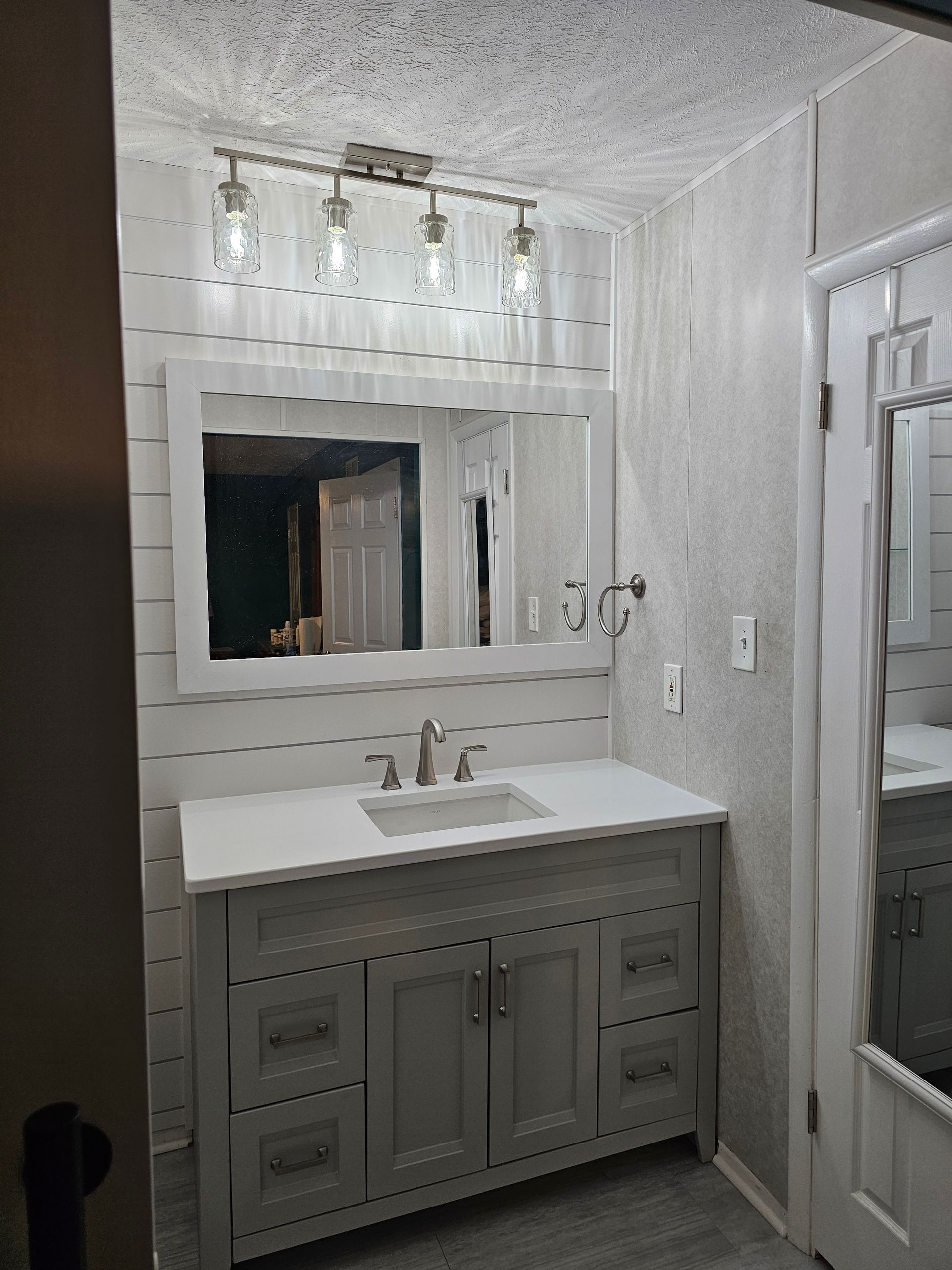 Bathroom with a gray vanity, white countertop, large mirror, and overhead light fixture.