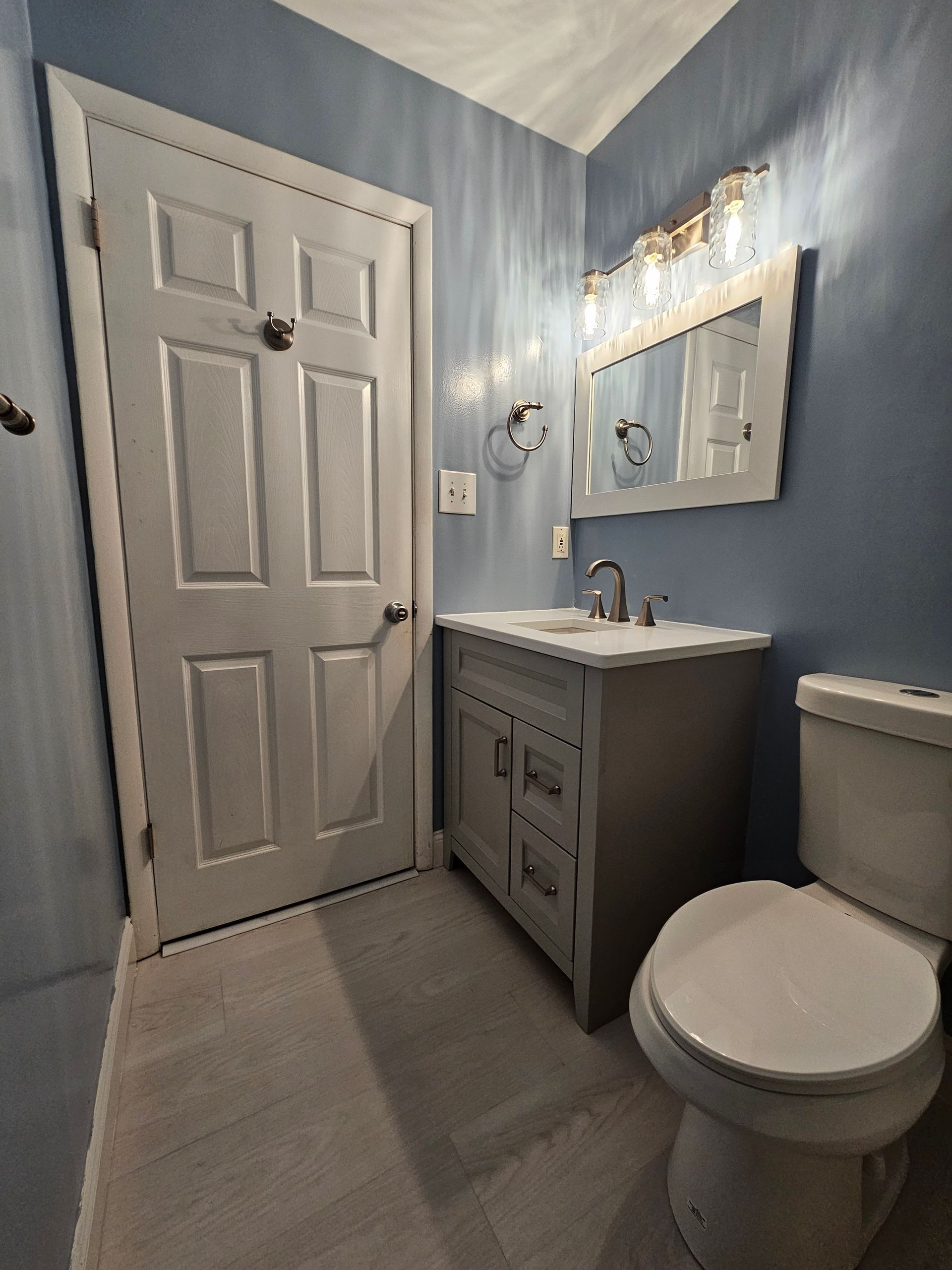 Bathroom with blue walls, gray vanity, toilet, and white door.