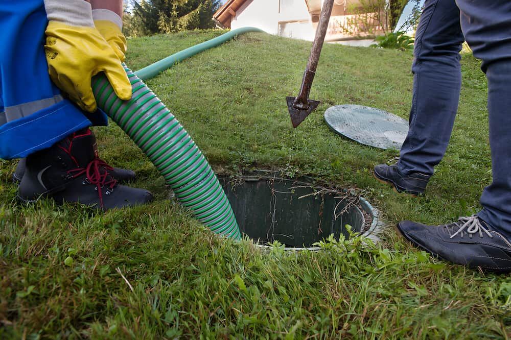 A Man Is Pumping Water Into A Septic Tank With A Green Hose — Gillen Plumbing In Ciccone, NT