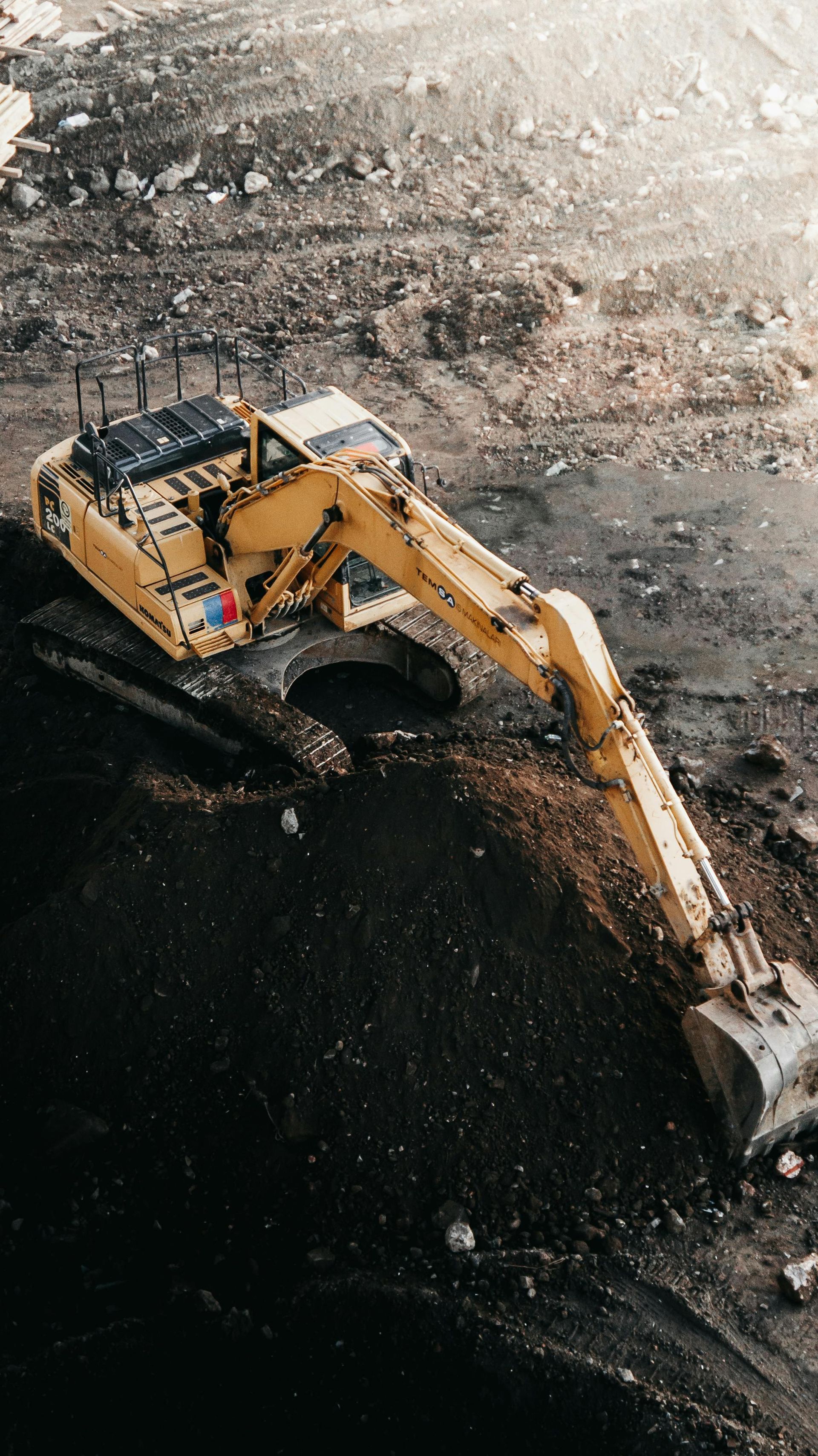 Yellow excavator digging a dark coal pile in a rocky mine site