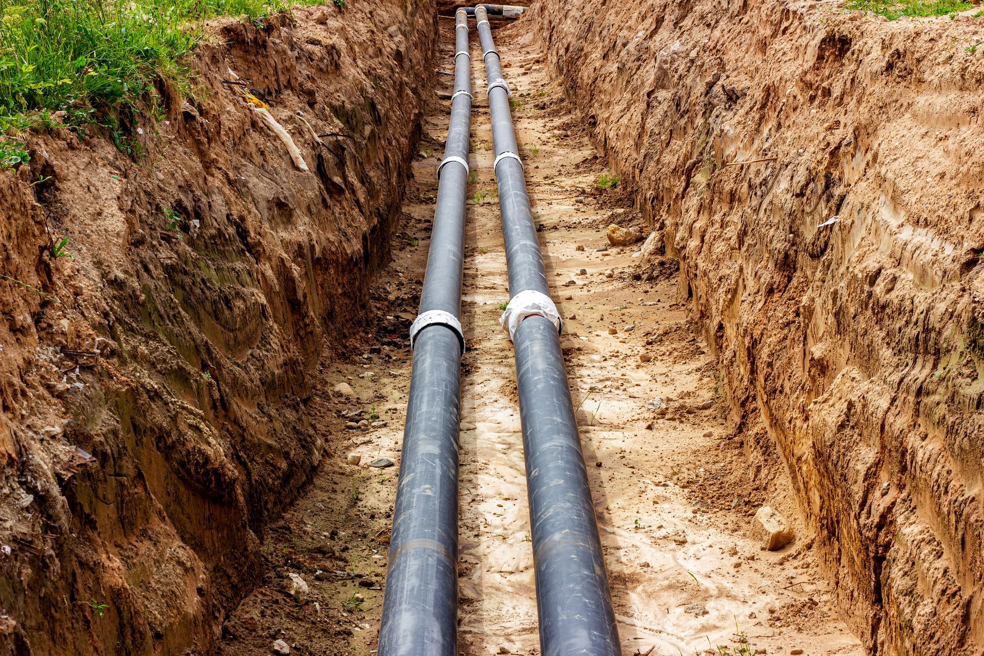 Two black utility pipes laid in a narrow dirt trench between excavated earth banks