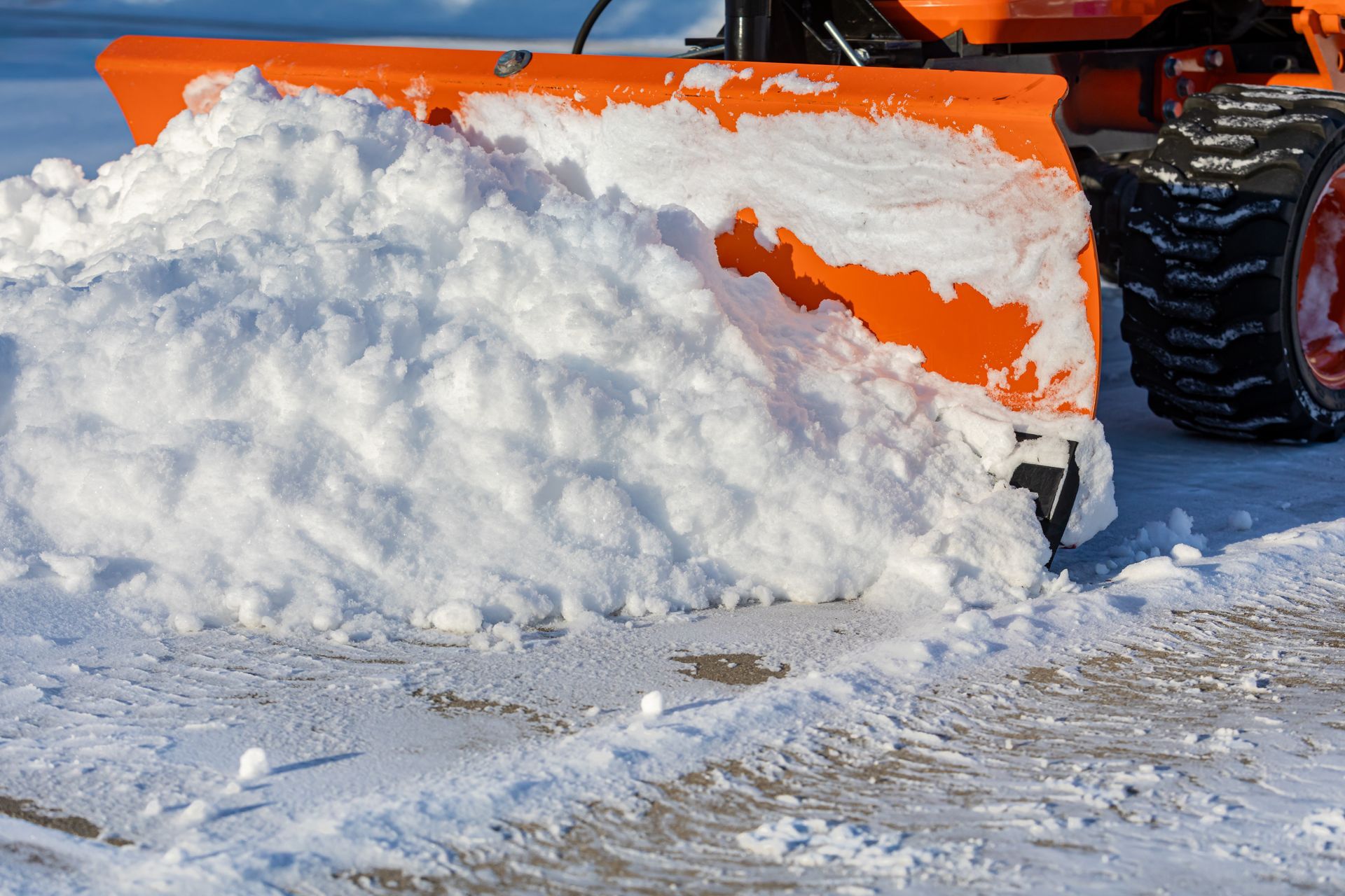 Orange snowplow pushing a pile of snow across a snowy road