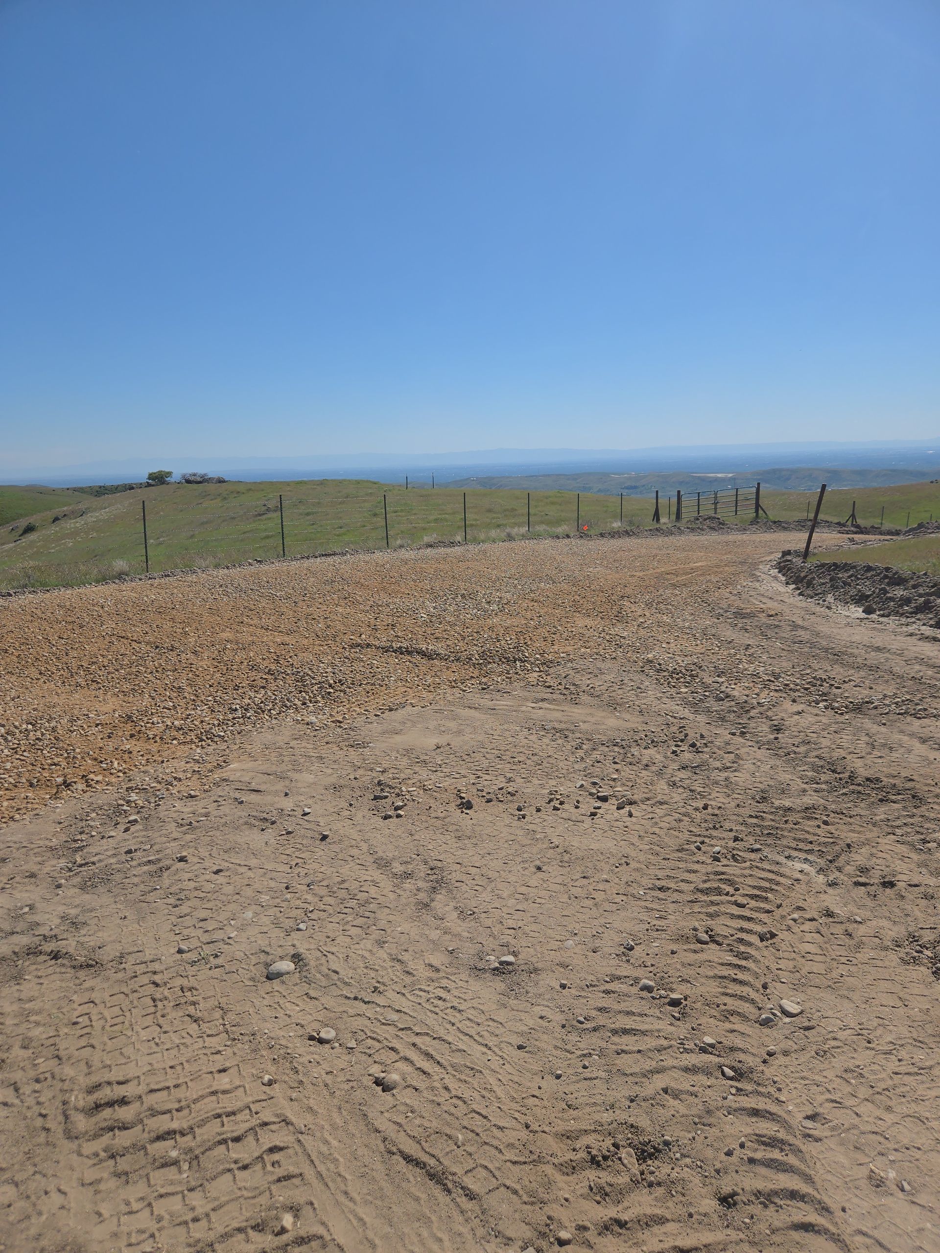Gravel path beside grassy fields under a clear blue sky, with fence posts in the distance