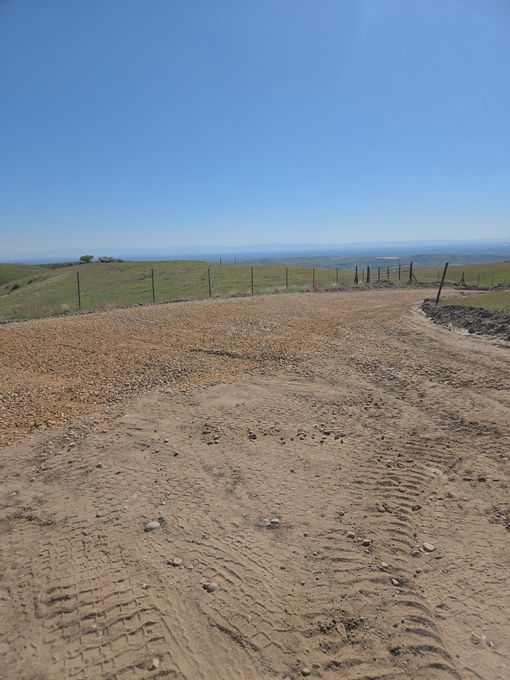 Gravel path beside grassy fields under a clear blue sky, with fence posts in the distance